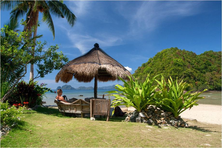 a girl sitting under umbrella in front of Las Cabanas beach in el nido