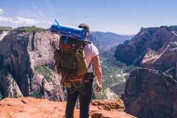 a man standing on the mountain with attaching sleeping bag to backpack